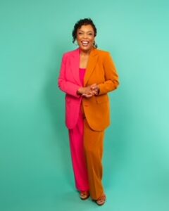 Dr. Renai Ellison posing with a green background in an orange and red pantsuit.